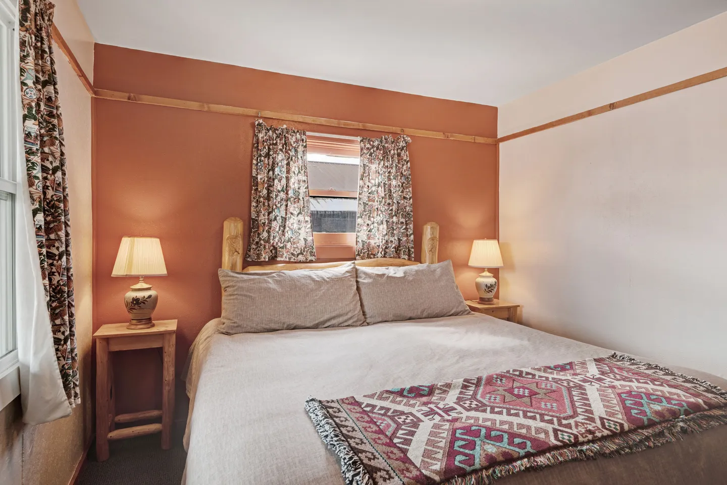 Bedroom featuring a made bed with a rustic log frame, warm orange accent wall, patterned throw blanket, and matching nightstands with lamps.