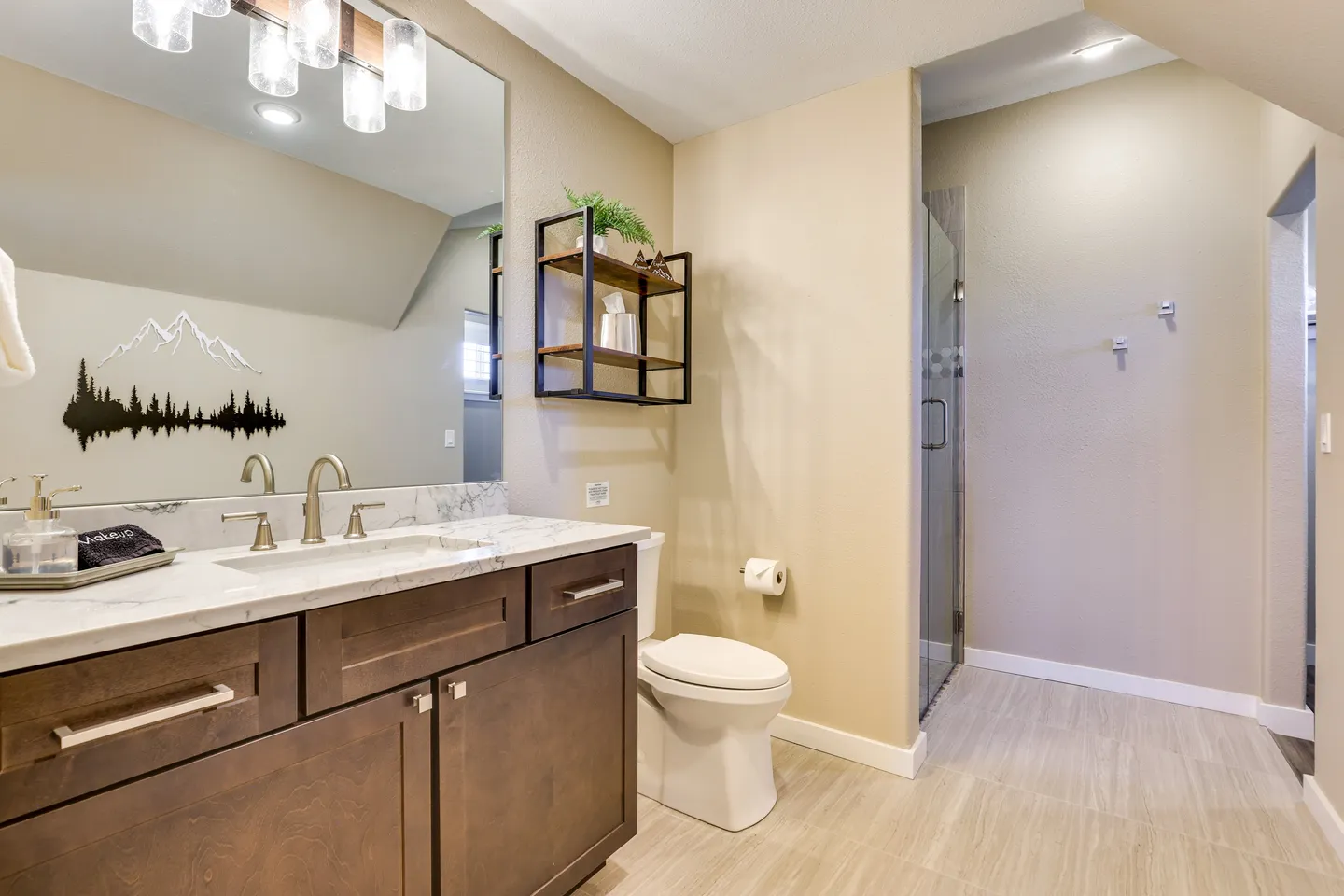 Bathroom with dark wood vanity, white marbled countertop, toilet, and walk-in shower with glass door.