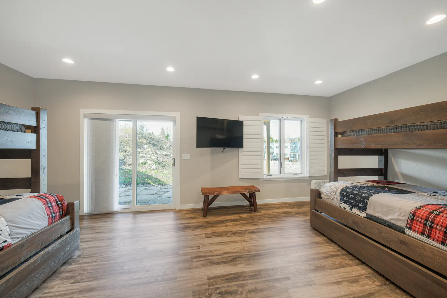 Spacious bedroom with wood-look flooring, two rustic wooden bunk beds, a wall-mounted TV, and sliding glass doors to the outside.