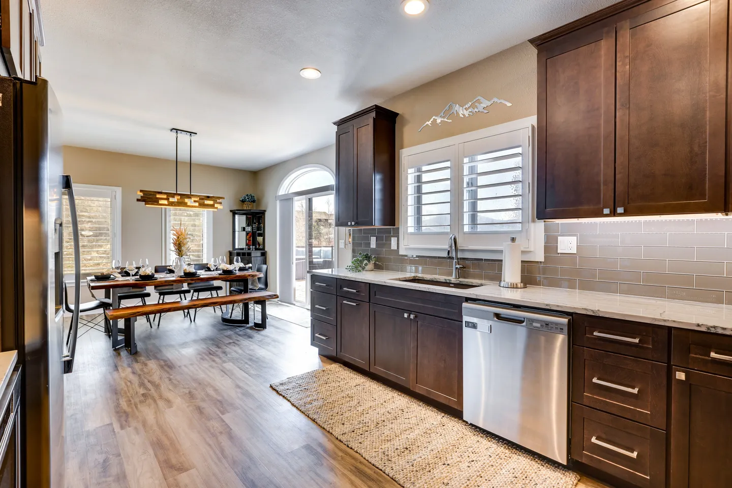 Open concept kitchen and dining area featuring dark wooden cabinets, stainless steel dishwasher, and a dining table with bench seating.