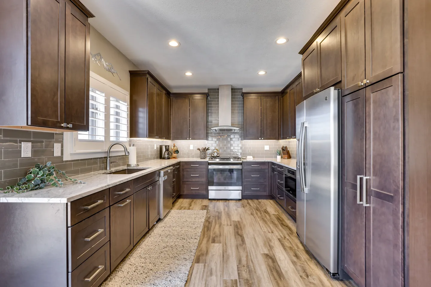 Spacious kitchen with dark wood cabinetry, stainless steel appliances, light countertops, and wood-look flooring.