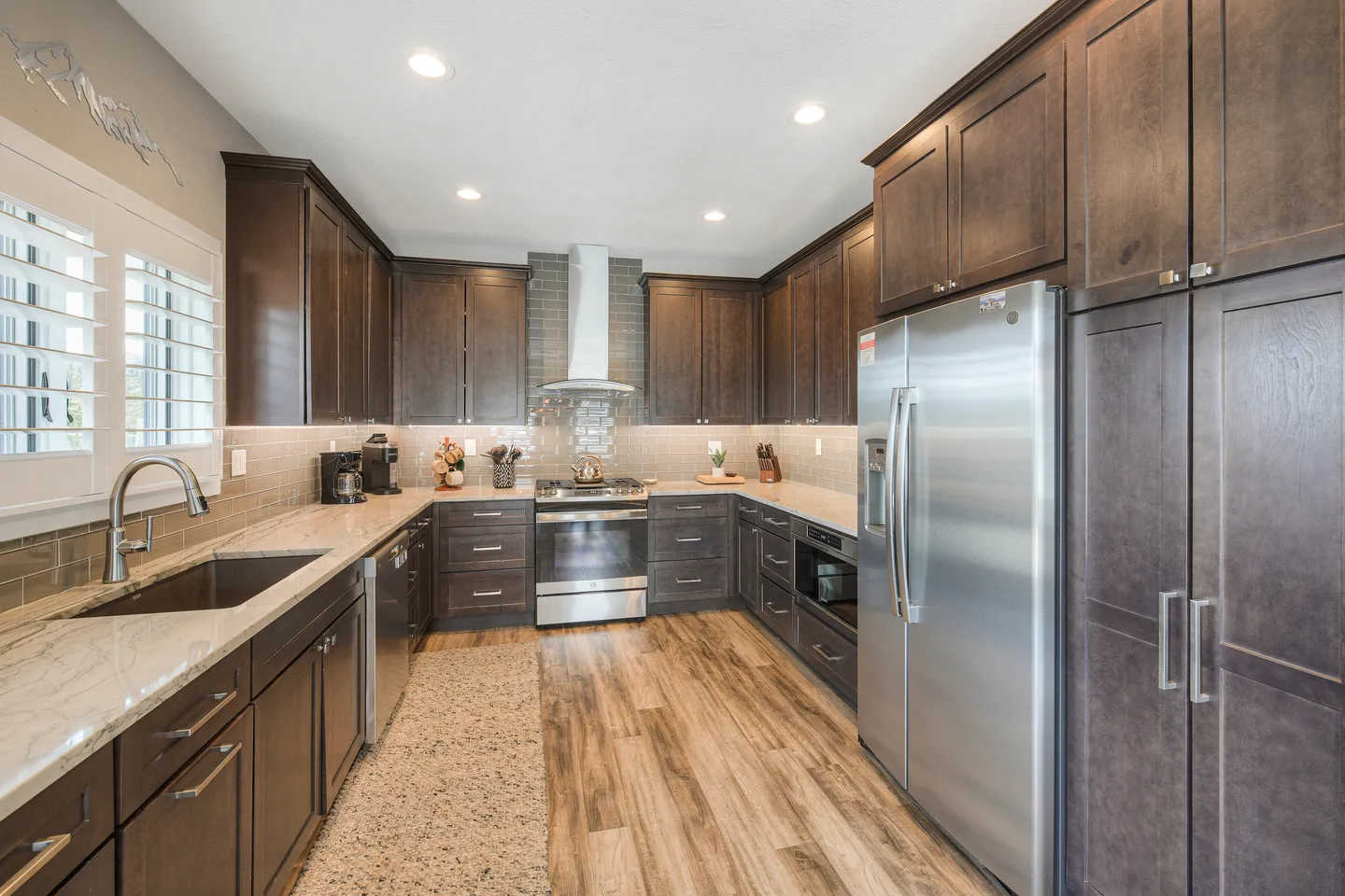 Spacious U-shaped kitchen with dark wood cabinets, stainless steel appliances, light countertops, and wood-look flooring.