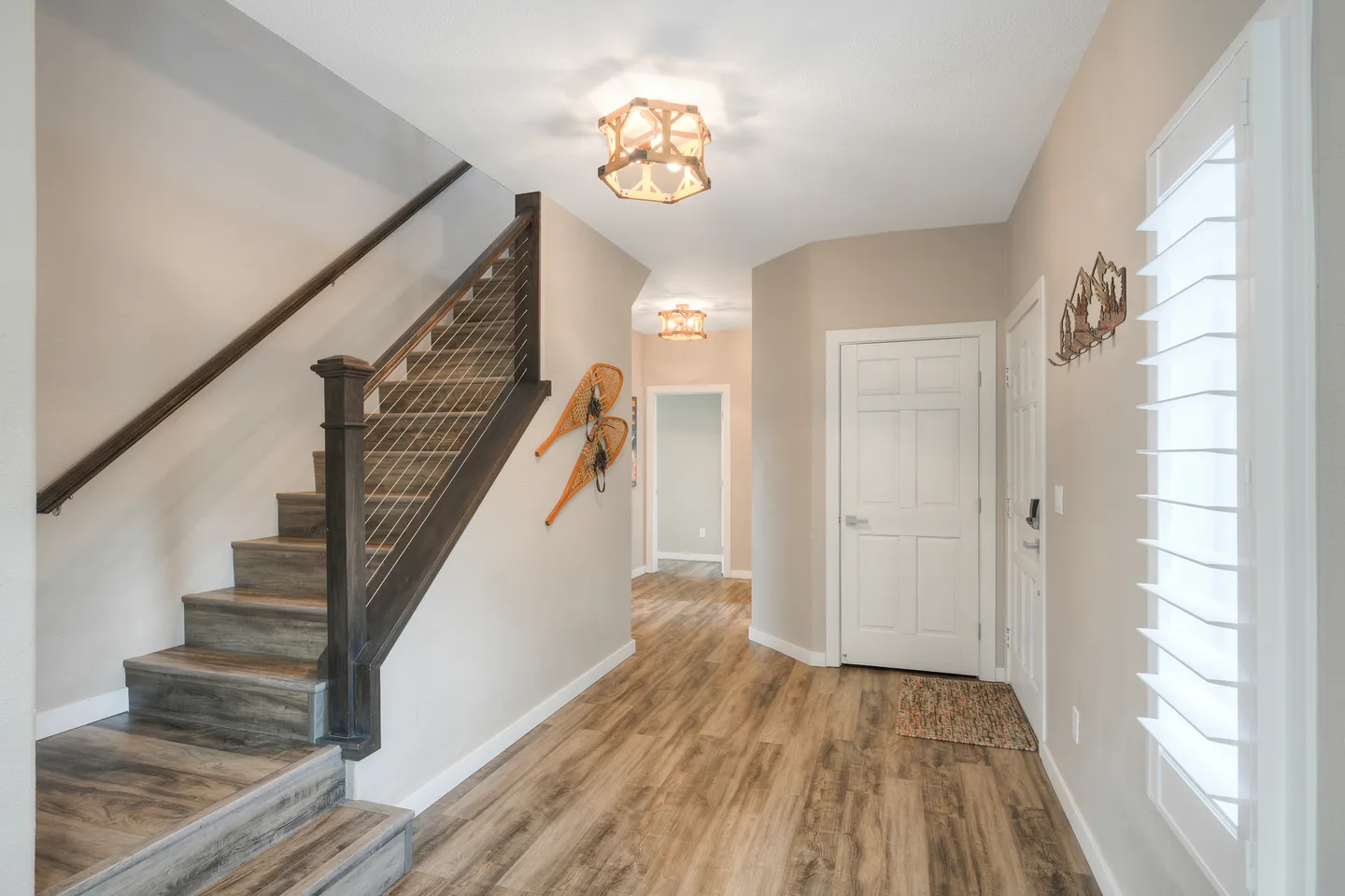 Entry hallway with wood-look flooring, a staircase with cable railings, white doors, and rustic wall decor.