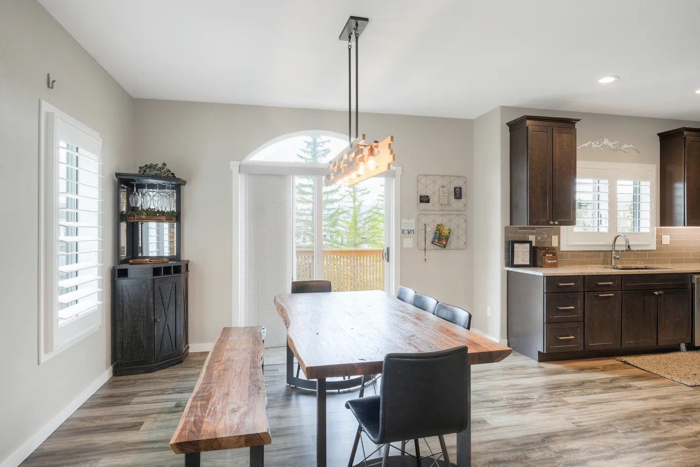Dining area with a live-edge wooden table, bench, and chairs adjacent to a kitchen and sliding glass door leading to a balcony.