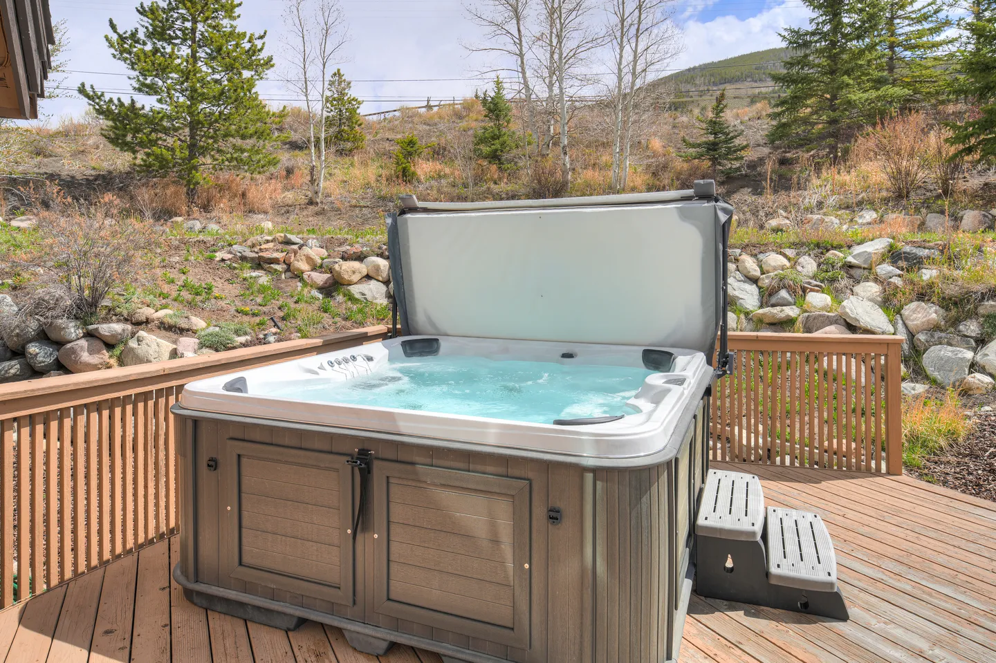 Outdoor hot tub filled with bubbling water on a wooden deck with hillside views.