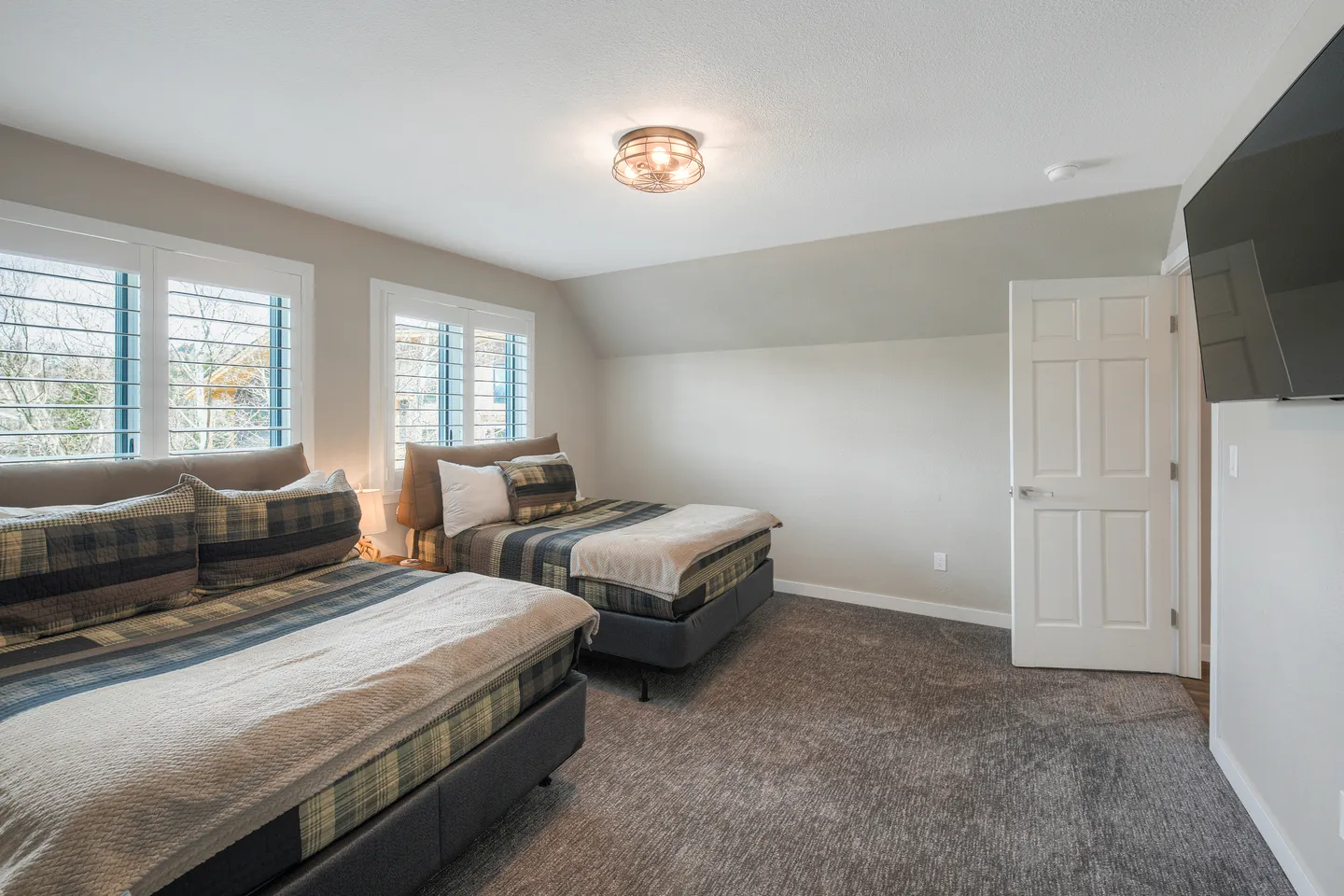 Bedroom with two beds, gray carpeting, shuttered windows, and a wall-mounted TV.