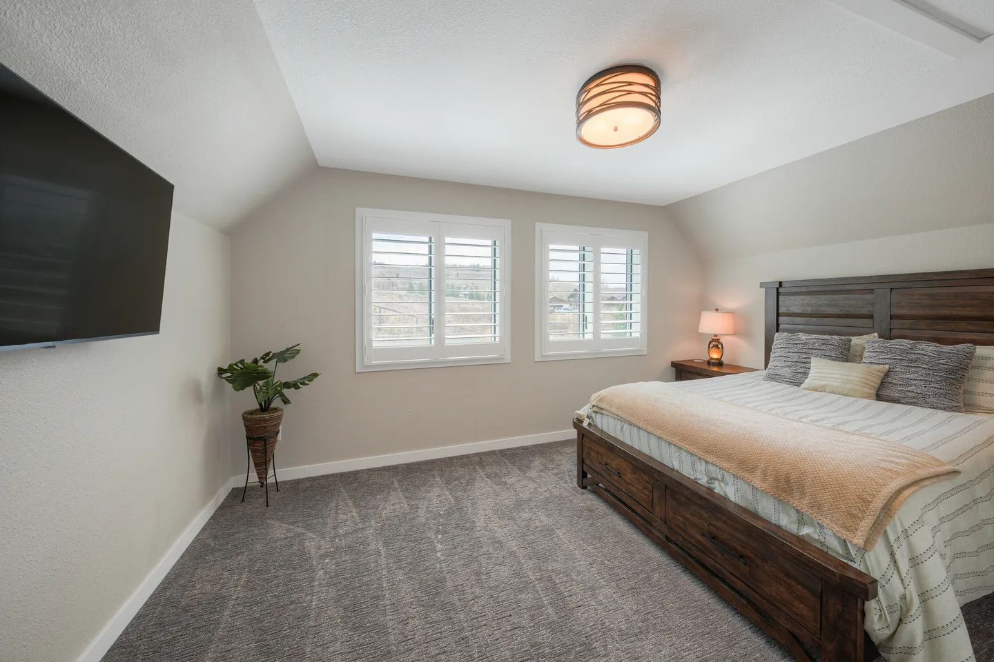 Bedroom featuring a wooden bed, wall-mounted television, carpeted floor, and shuttered windows.