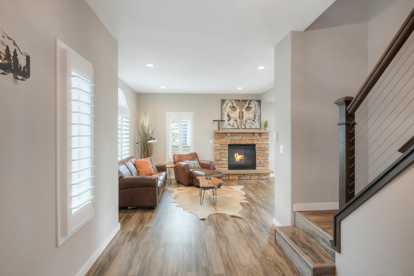 Hallway view into a living room featuring a stone fireplace with a fire lit, leather seating, wood-look flooring, and a hide rug.