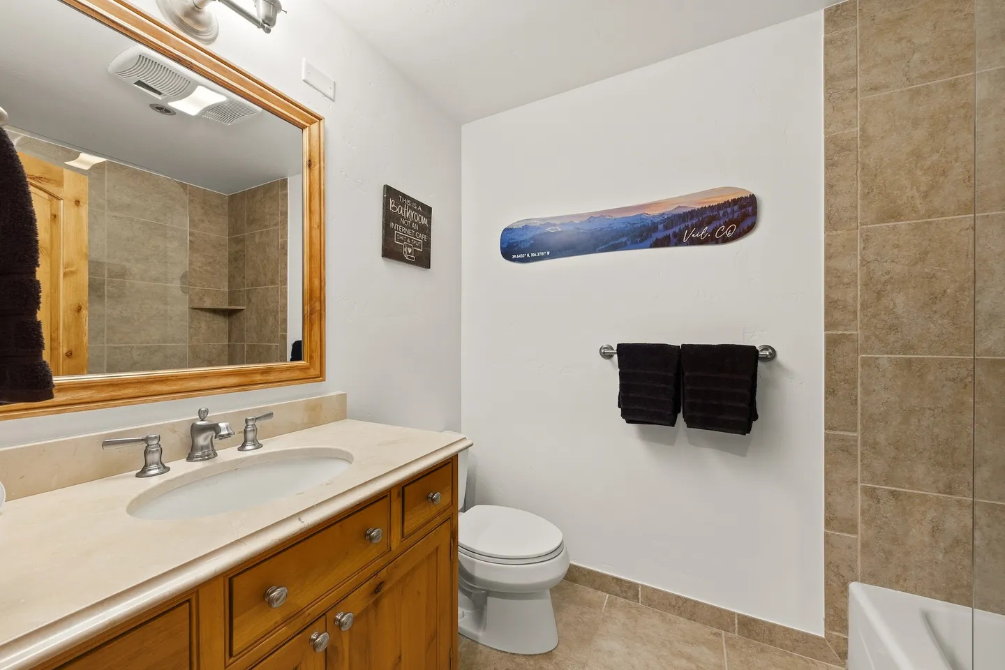 Bathroom with a wood vanity, large mirror, toilet, towel bar, and tiled shower edge.