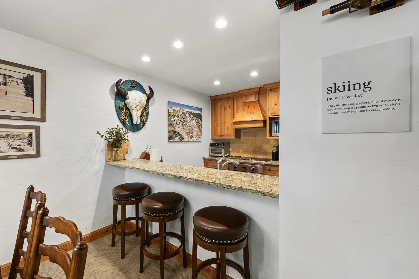 Kitchen counter breakfast bar with three brown leather barstools adjacent to a dining area and wood-paneled kitchen.