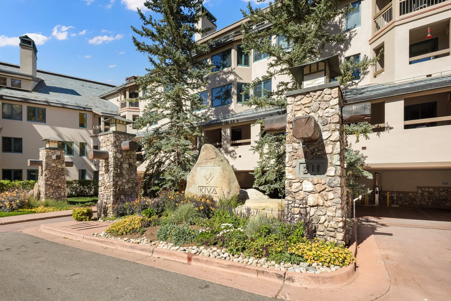 Exterior entrance of Kiva lodge featuring stone pillars, landscaped flower beds, and a large engraved boulder.
