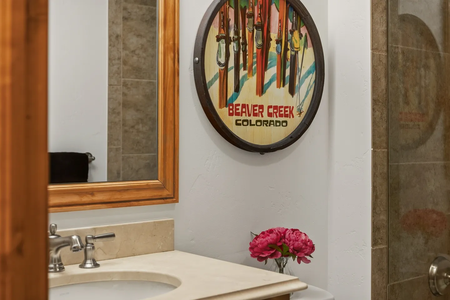 Bathroom vanity counter with sink, wooden framed mirror, and a circular Beaver Creek Colorado ski sign on the wall.