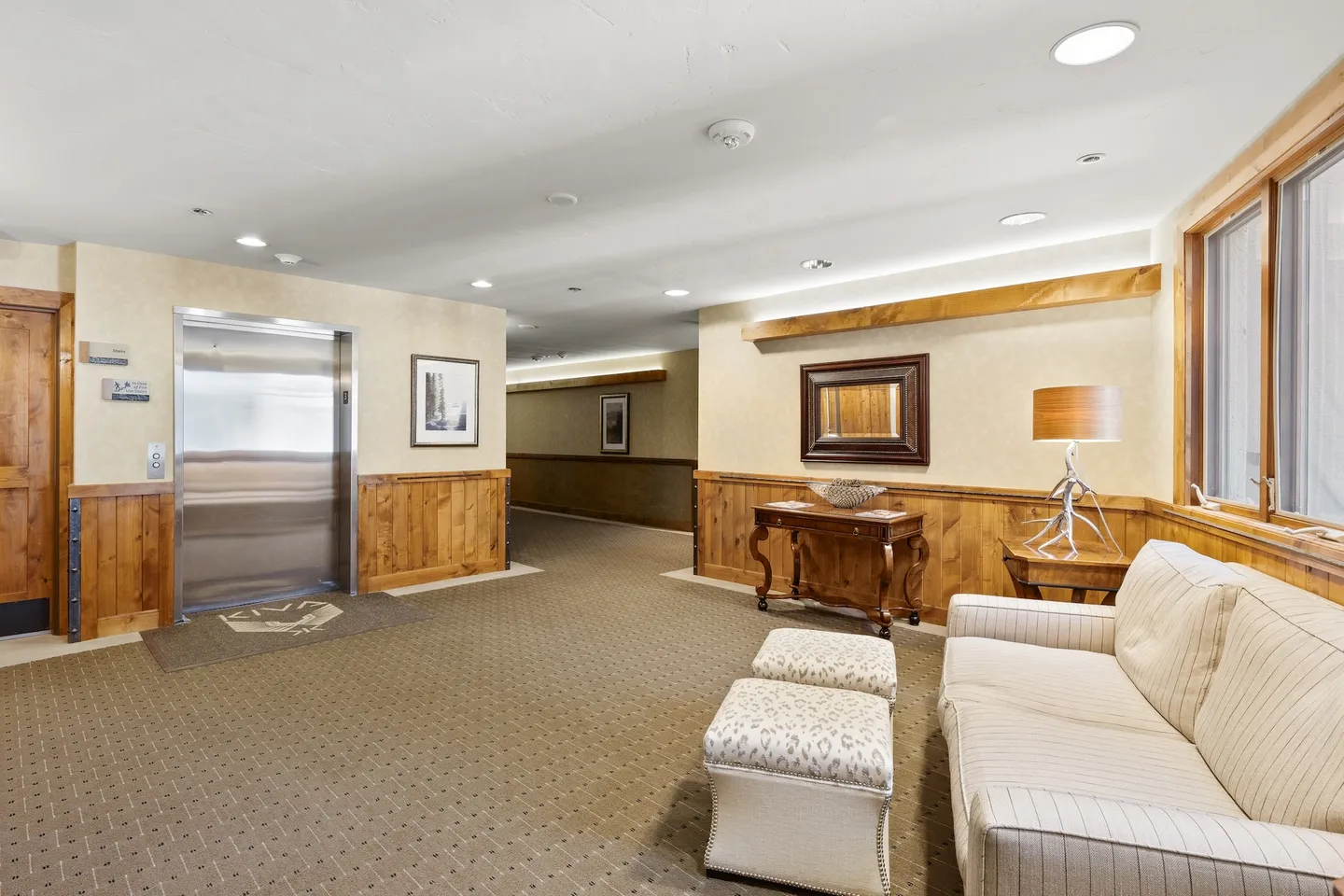 Building lobby and elevator area with carpeted floors, wood wainscoting, an elevator, sofa, and hallway.