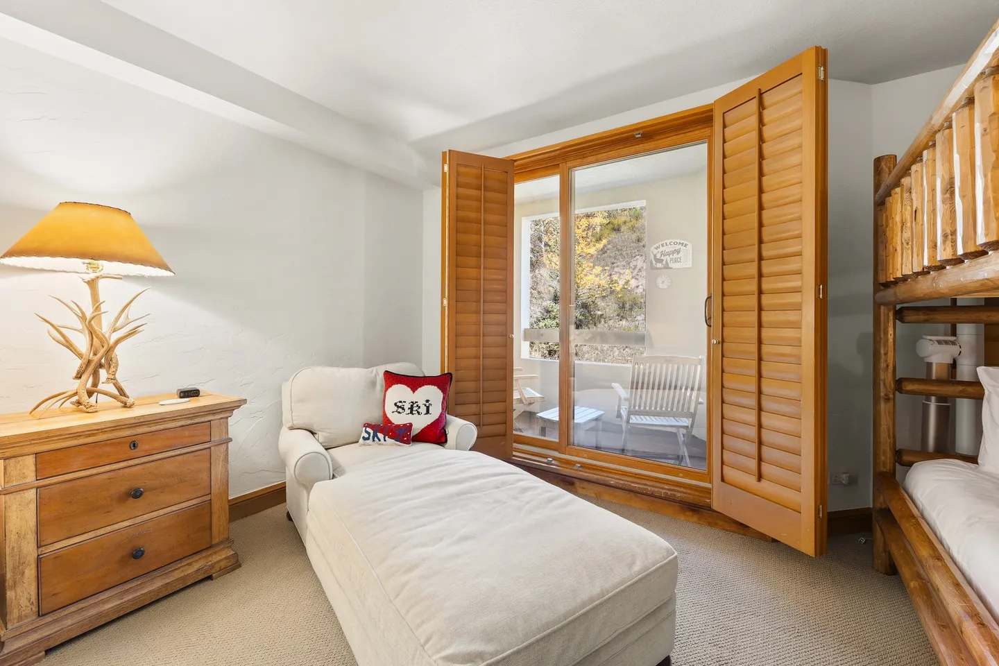 Bedroom with a chaise lounge, wooden dresser, log-style bunk bed, and open wooden shutter doors leading to a patio.
