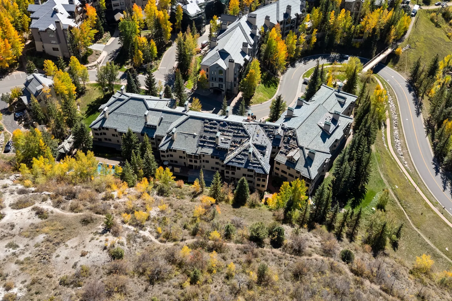 Aerial view of a large multi-story mountain lodge complex surrounded by autumn trees and winding roads.