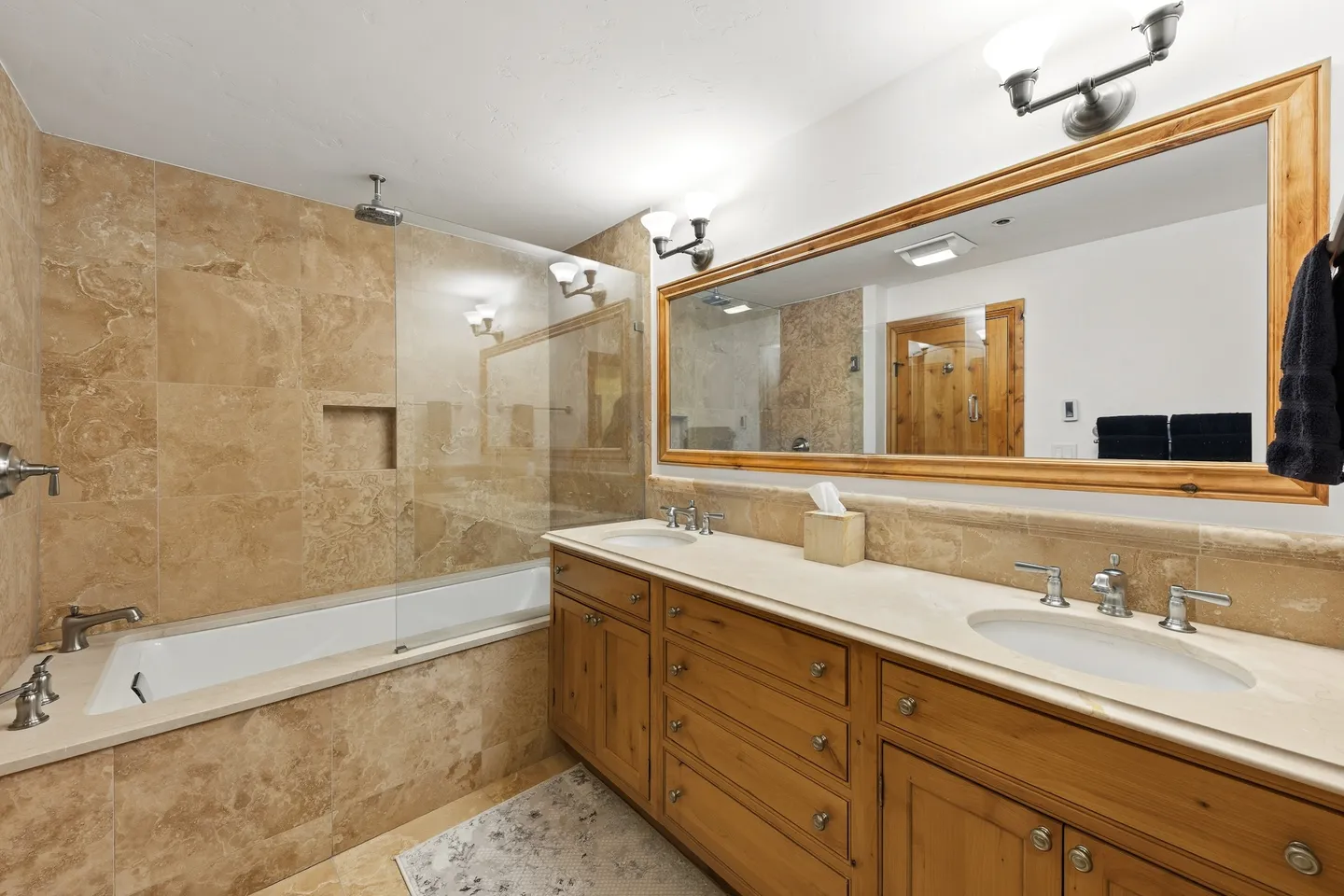 Bathroom with a long wood double vanity, large wood-framed mirror, and a tiled bathtub and shower combination.