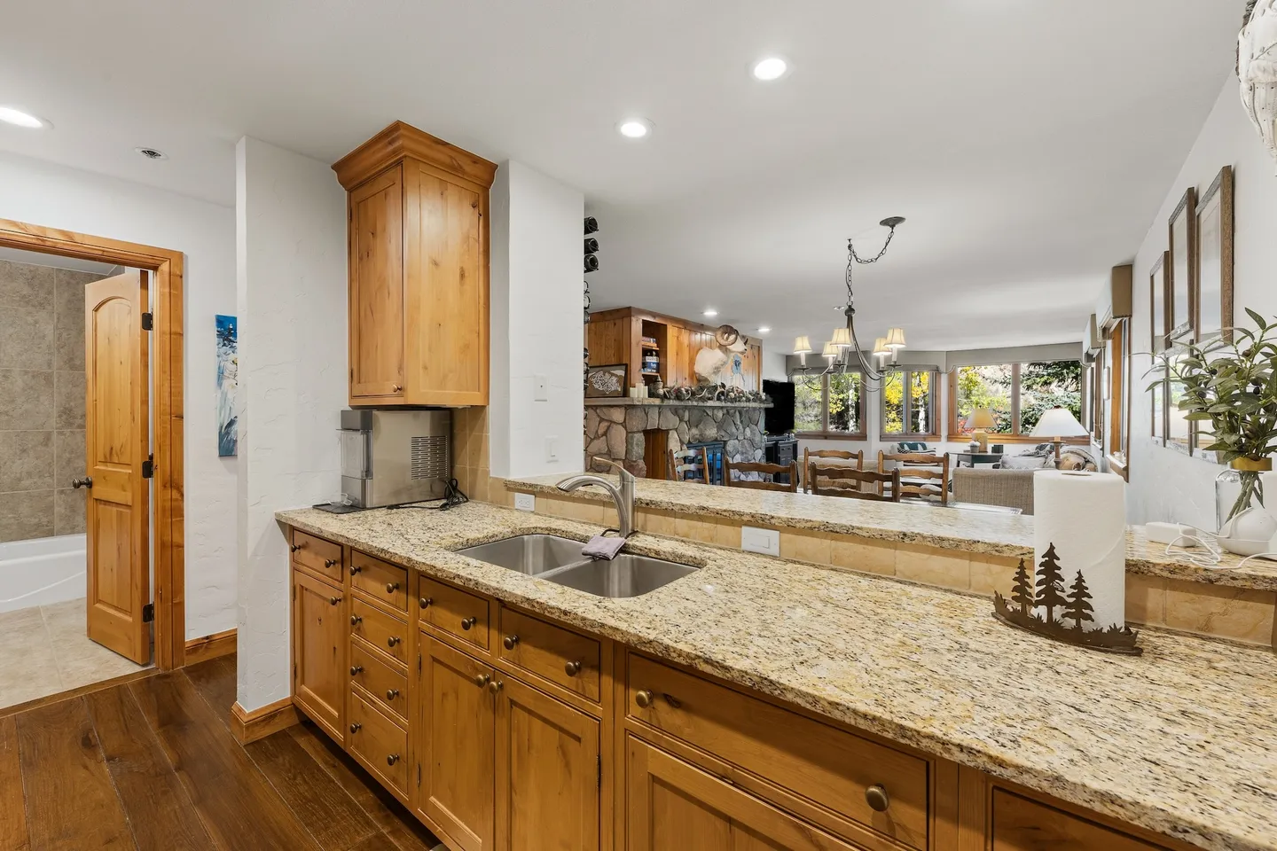 Kitchen counter with stainless steel sink and granite countertop looking toward the open living area with stone fireplace and an adjoining bathroom.