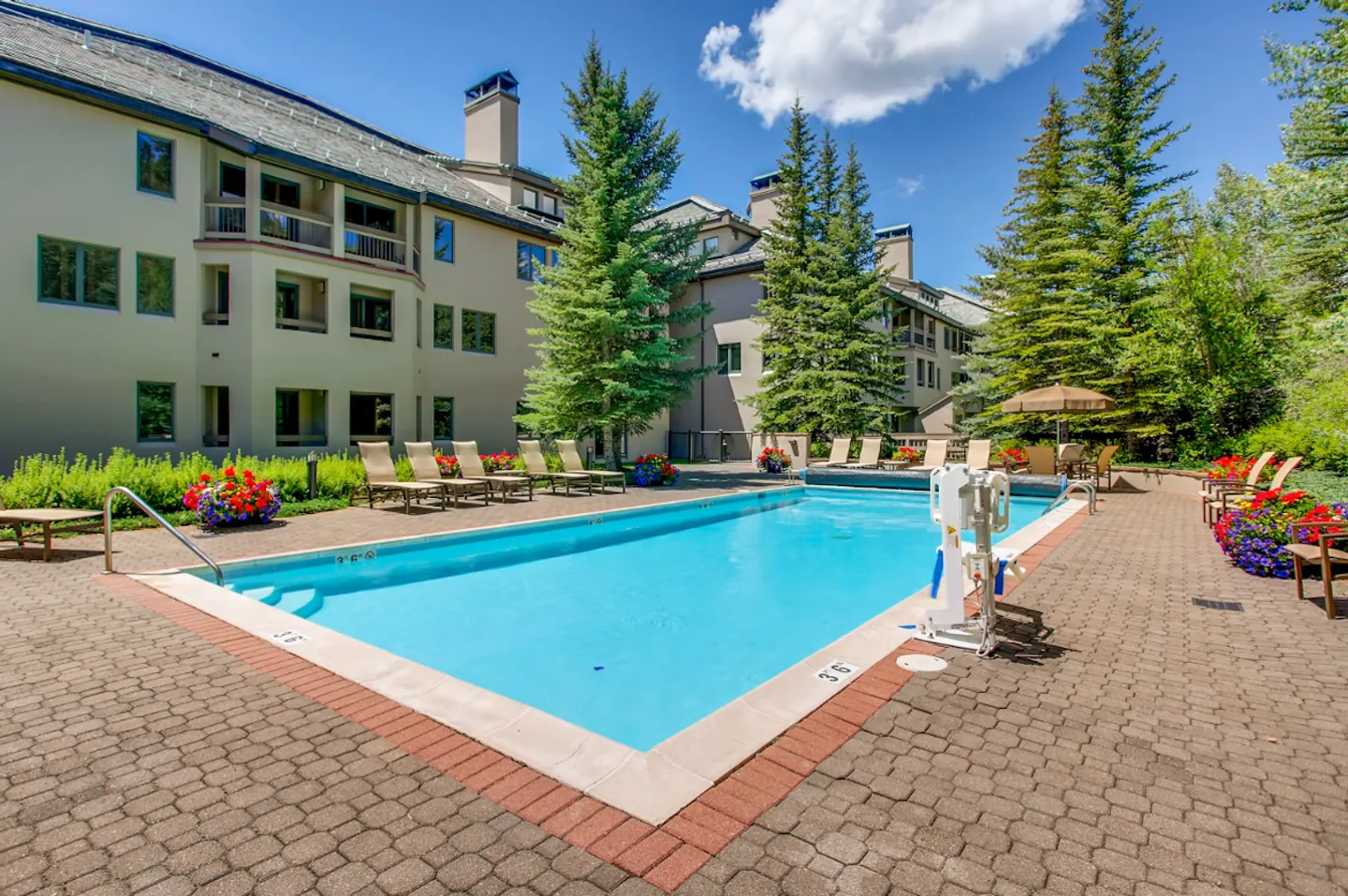 Outdoor swimming pool surrounded by a brick paver patio, lounge chairs, and a multi-story residential building.