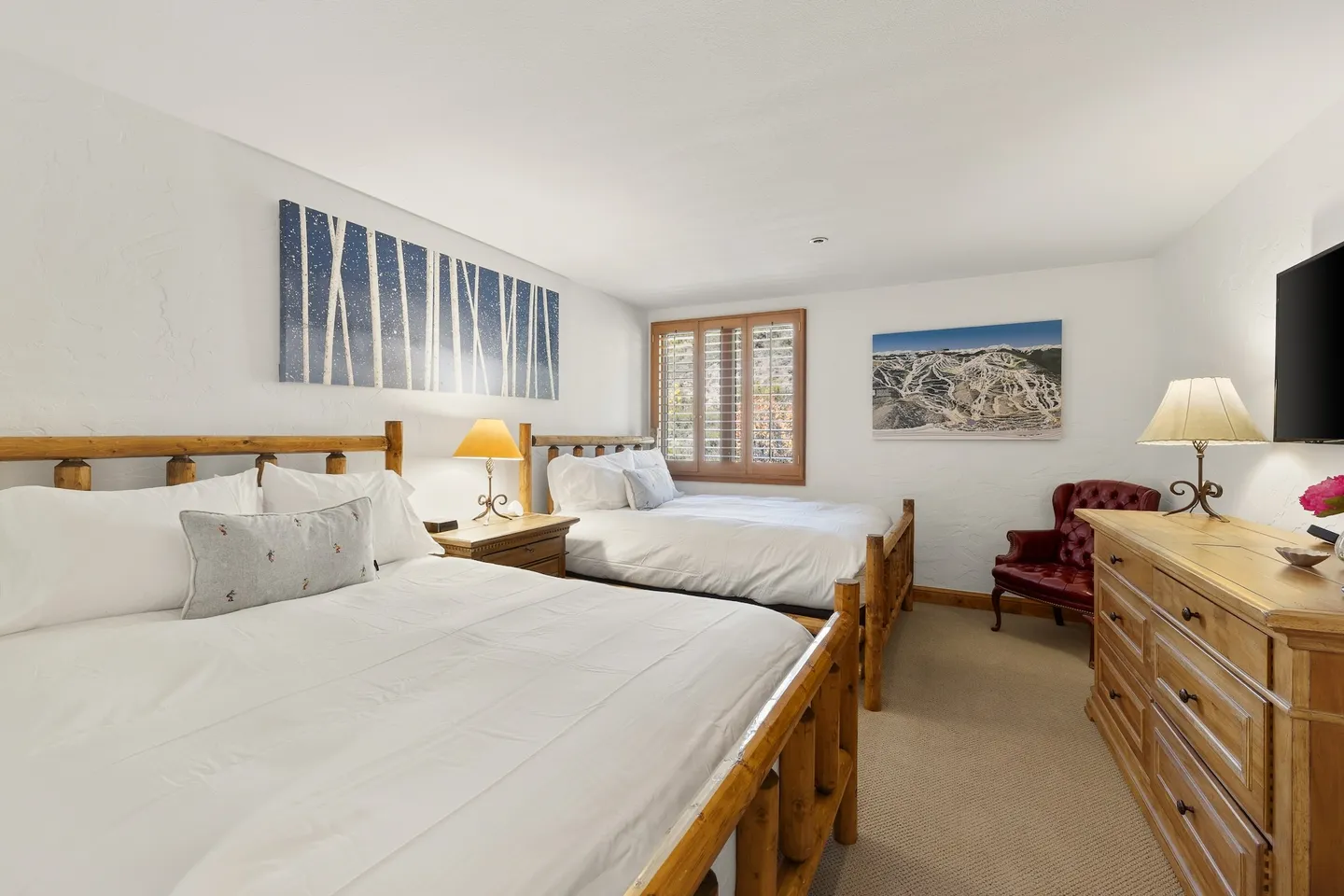 Bedroom with two wooden log-style beds, a wood dresser, an armchair, and artwork on the white walls.