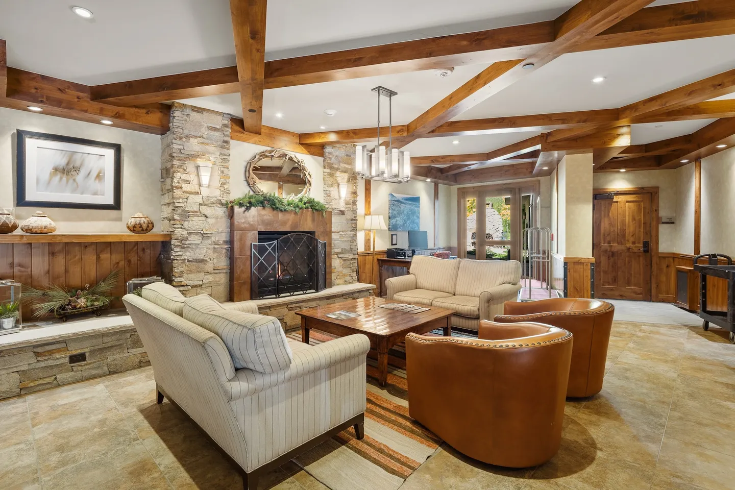 Lobby or common seating area with exposed wood ceiling beams, a stone fireplace, couches, and leather armchairs.