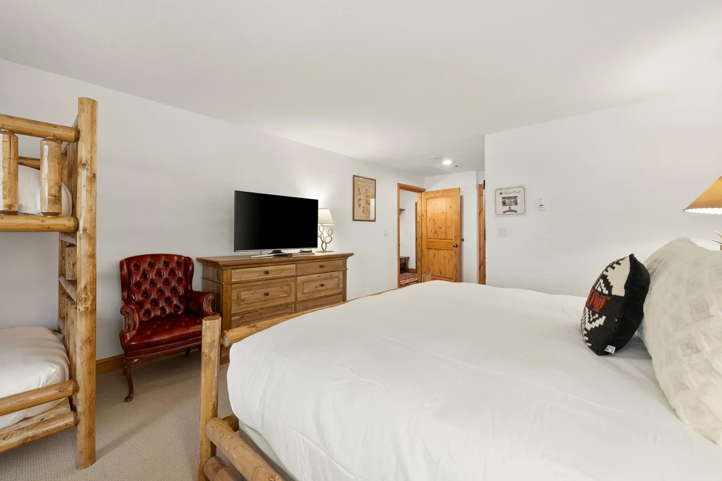 Bedroom with a large bed, log bunk beds, a tufted armchair, and a TV on a wooden dresser.