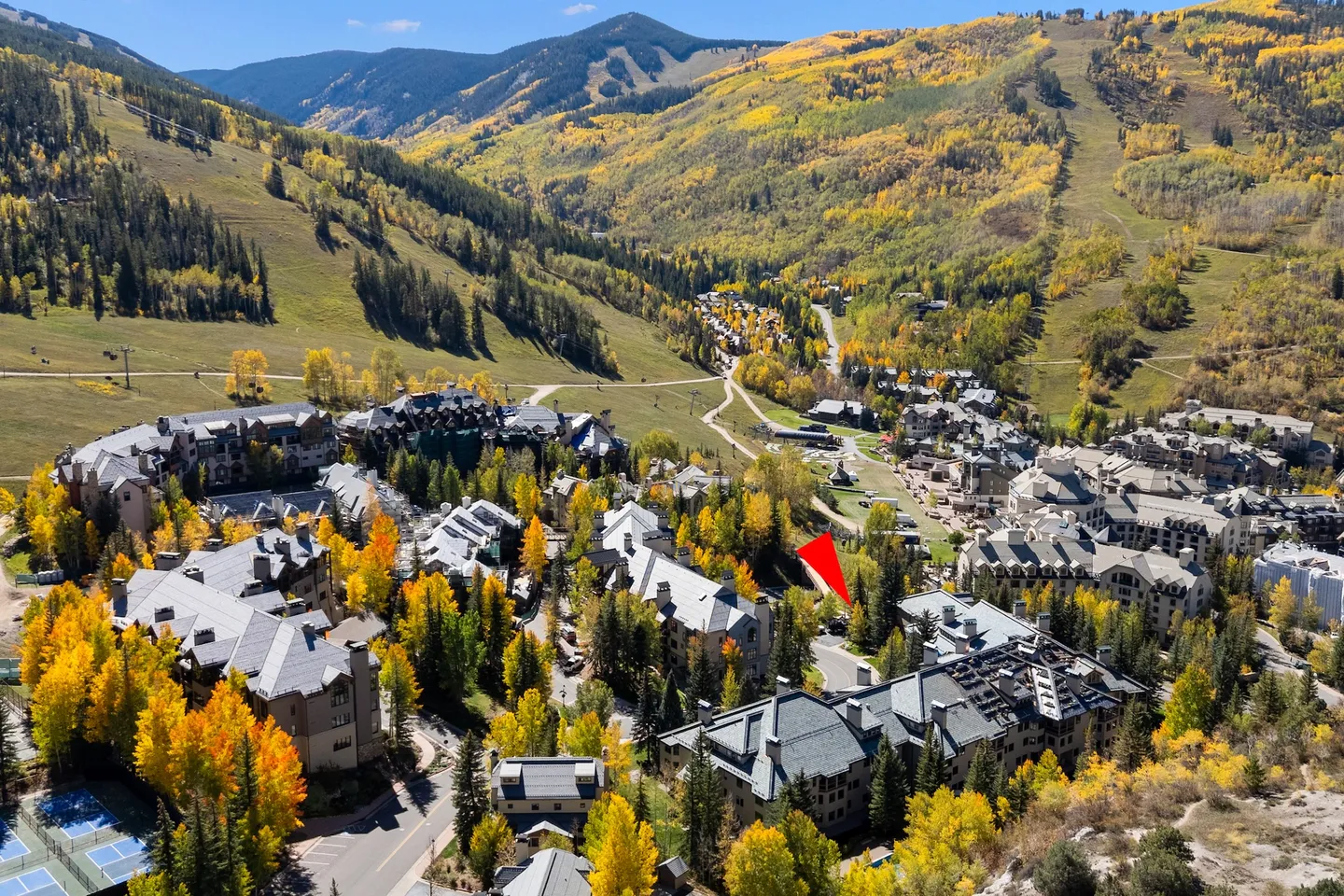 Aerial view of a mountain village surrounded by hills covered in autumn foliage, with a red arrow pointing to a property.
