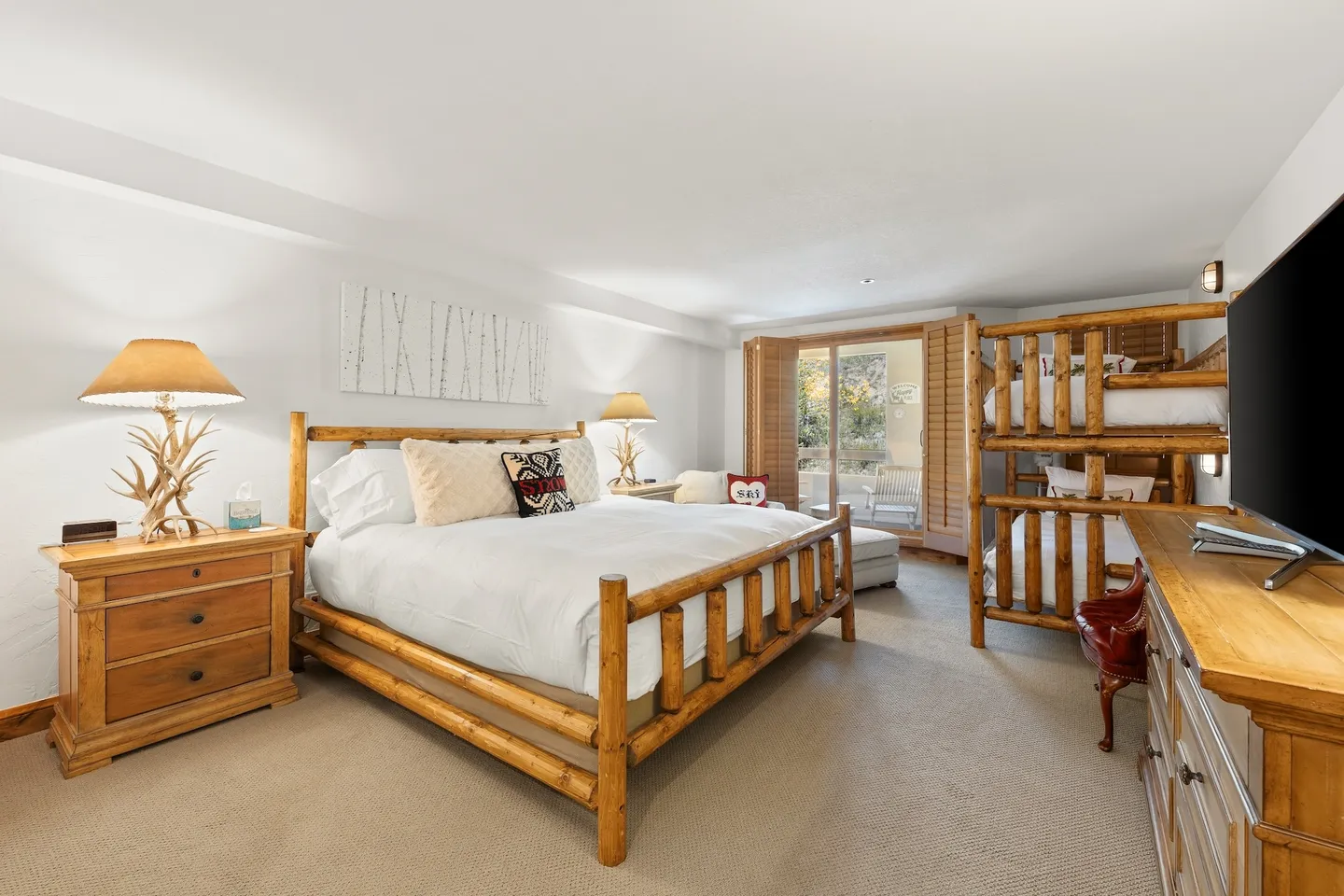 Bedroom featuring a log-style bed, matching nightstands, a set of bunk beds, and a patio door with wooden shutters.