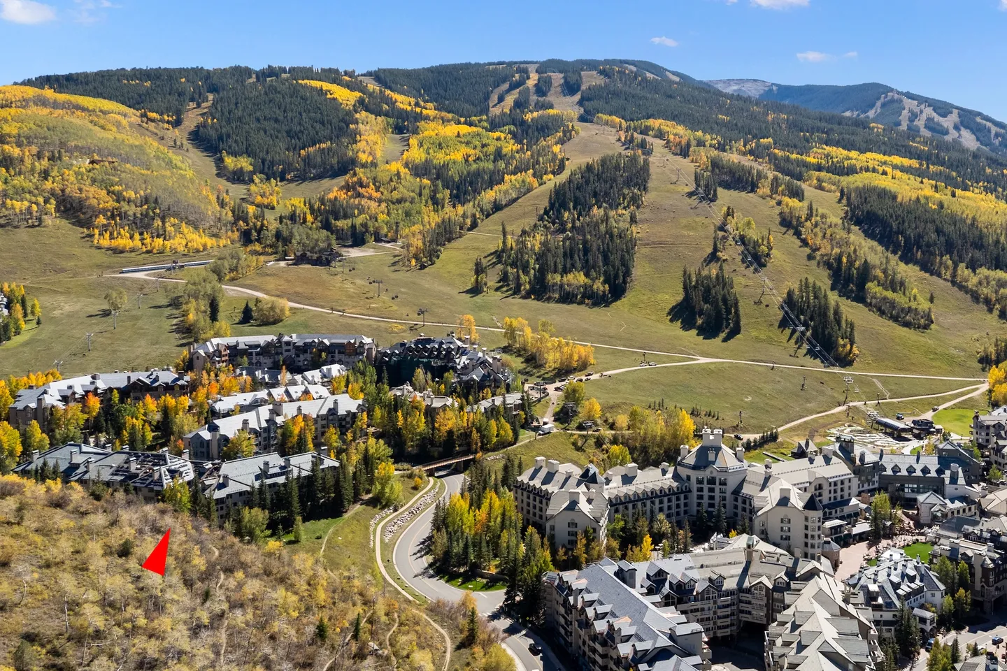 Aerial view of a mountain resort village surrounded by fall foliage, ski slopes, and forested hills.