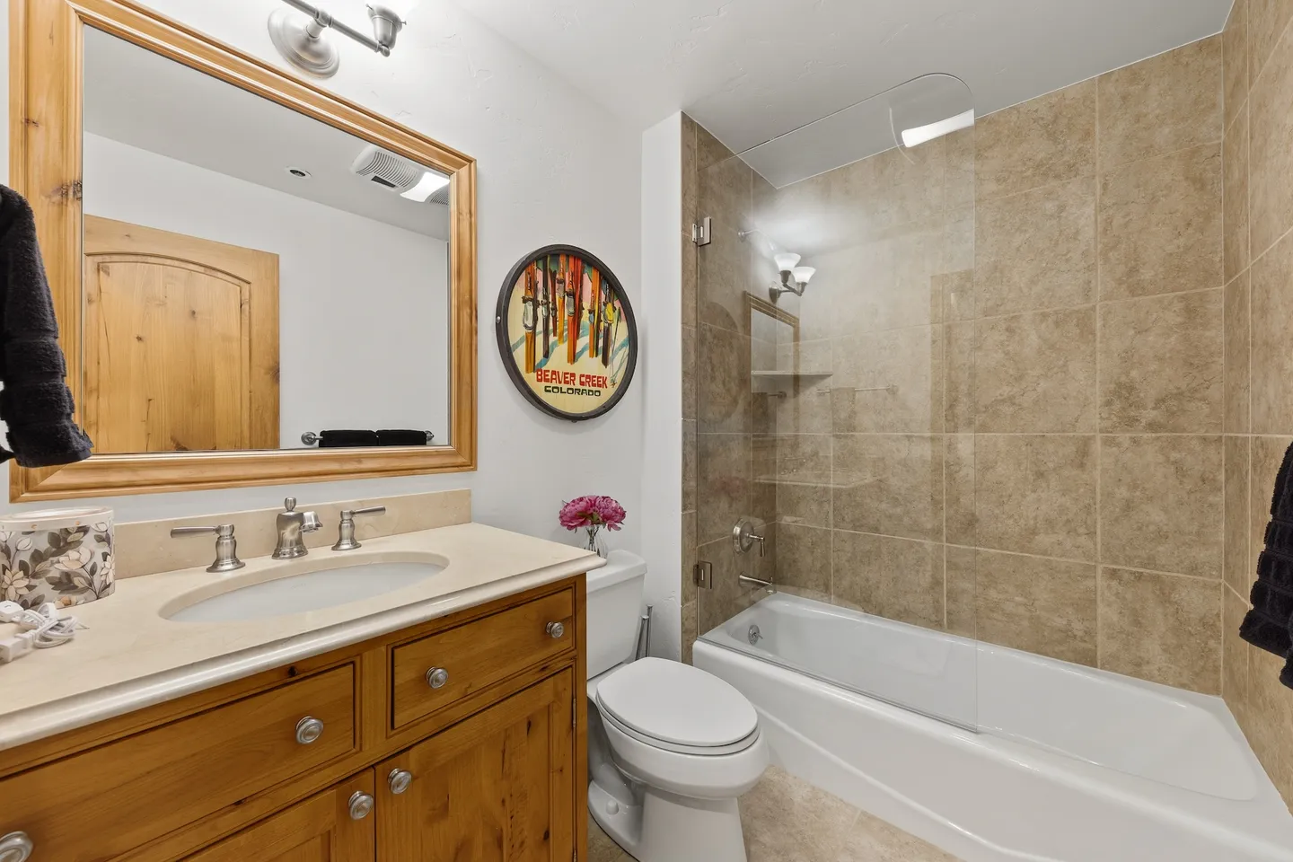 Bathroom with a wood vanity, framed mirror, toilet, and combination bathtub and shower with beige tile surround.