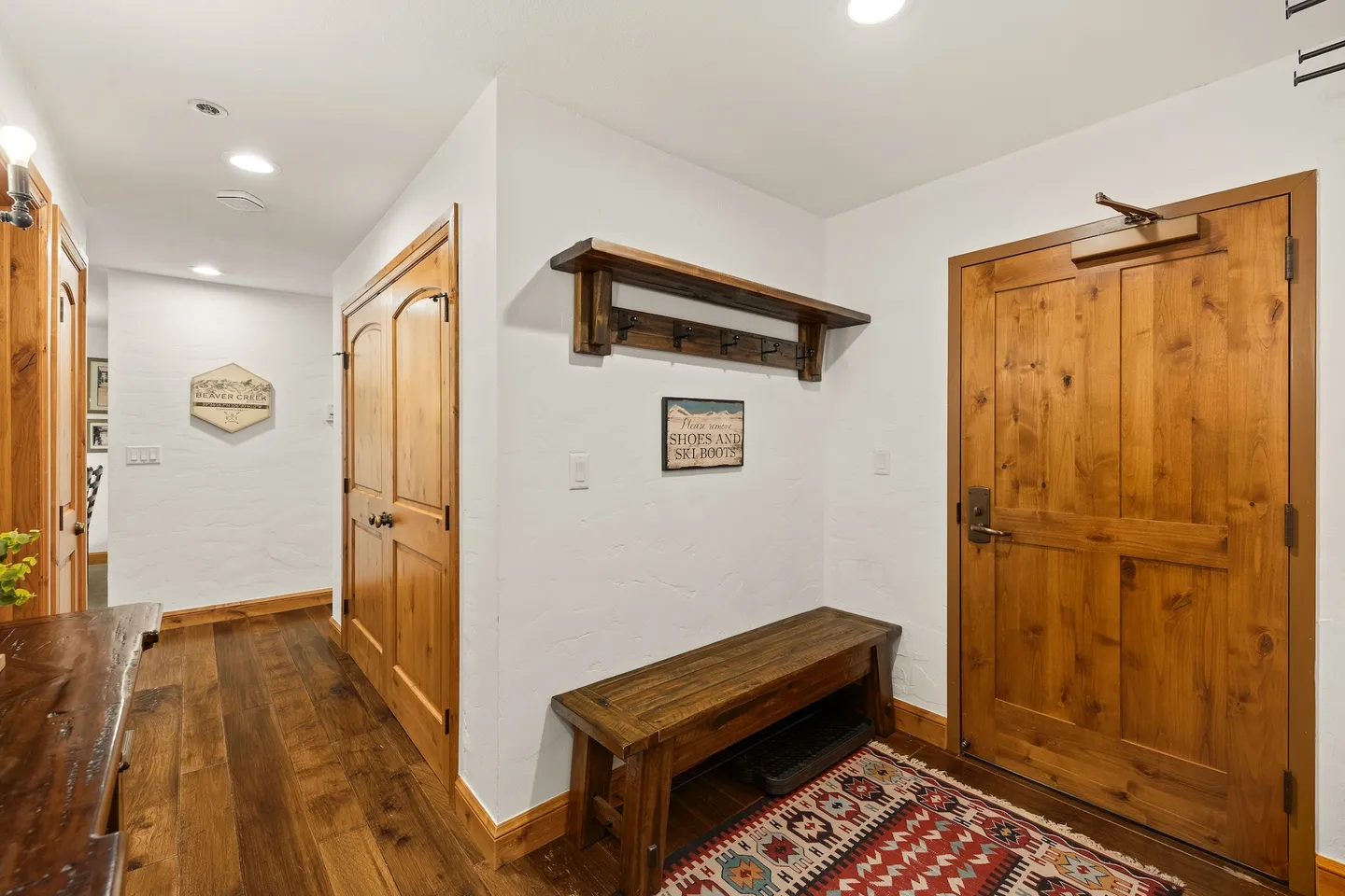 Entryway with a wooden front door, a dark wood bench, coat hooks on a wall shelf, and wood flooring.