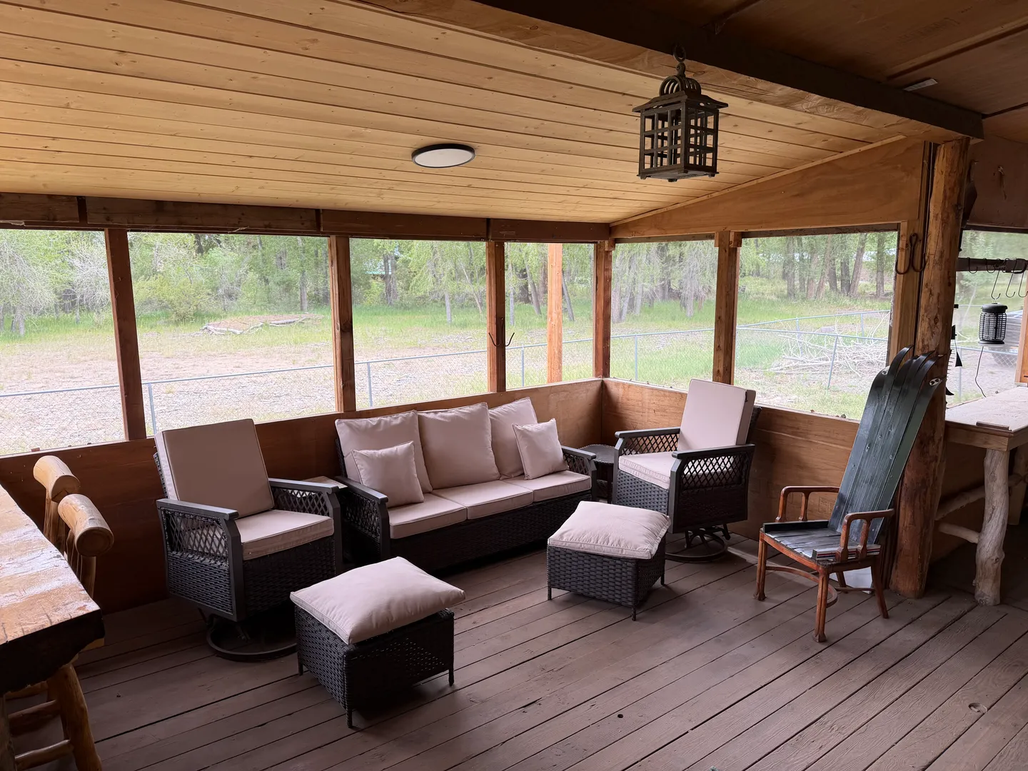 Screened-in porch with wood-paneled ceiling, wood floor, and outdoor seating set overlooking trees.