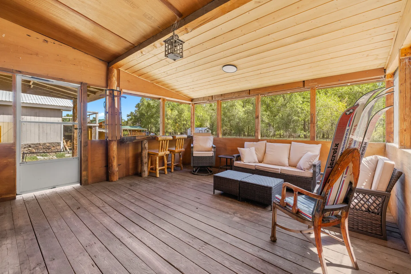 Screened-in porch with wood-plank flooring, wood-paneled ceiling, and an outdoor seating area with sofas, chairs, and barstools.