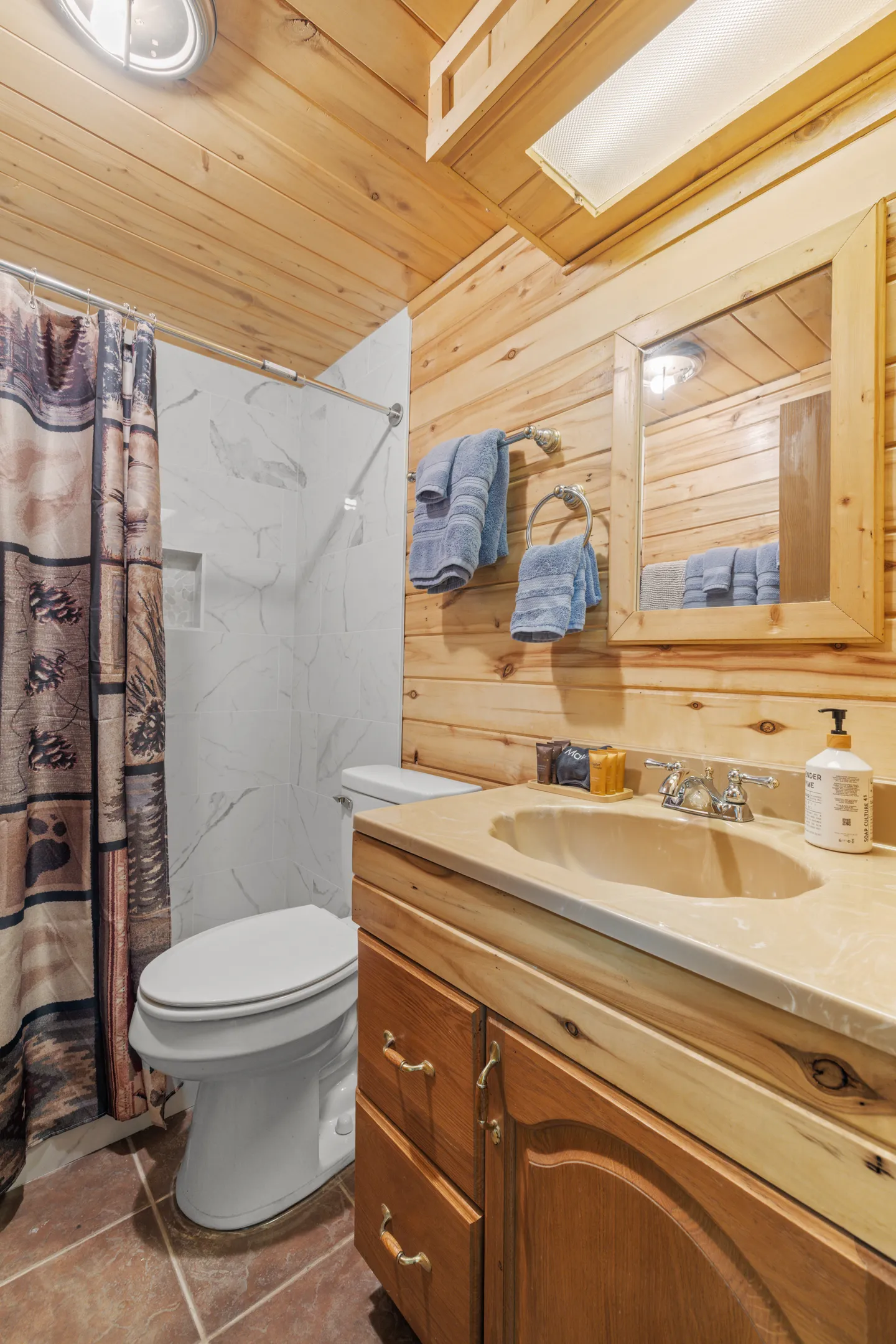 Bathroom with wood-paneled walls and ceiling, a wooden vanity with sink, a white toilet, and a tiled shower stall with a curtain.