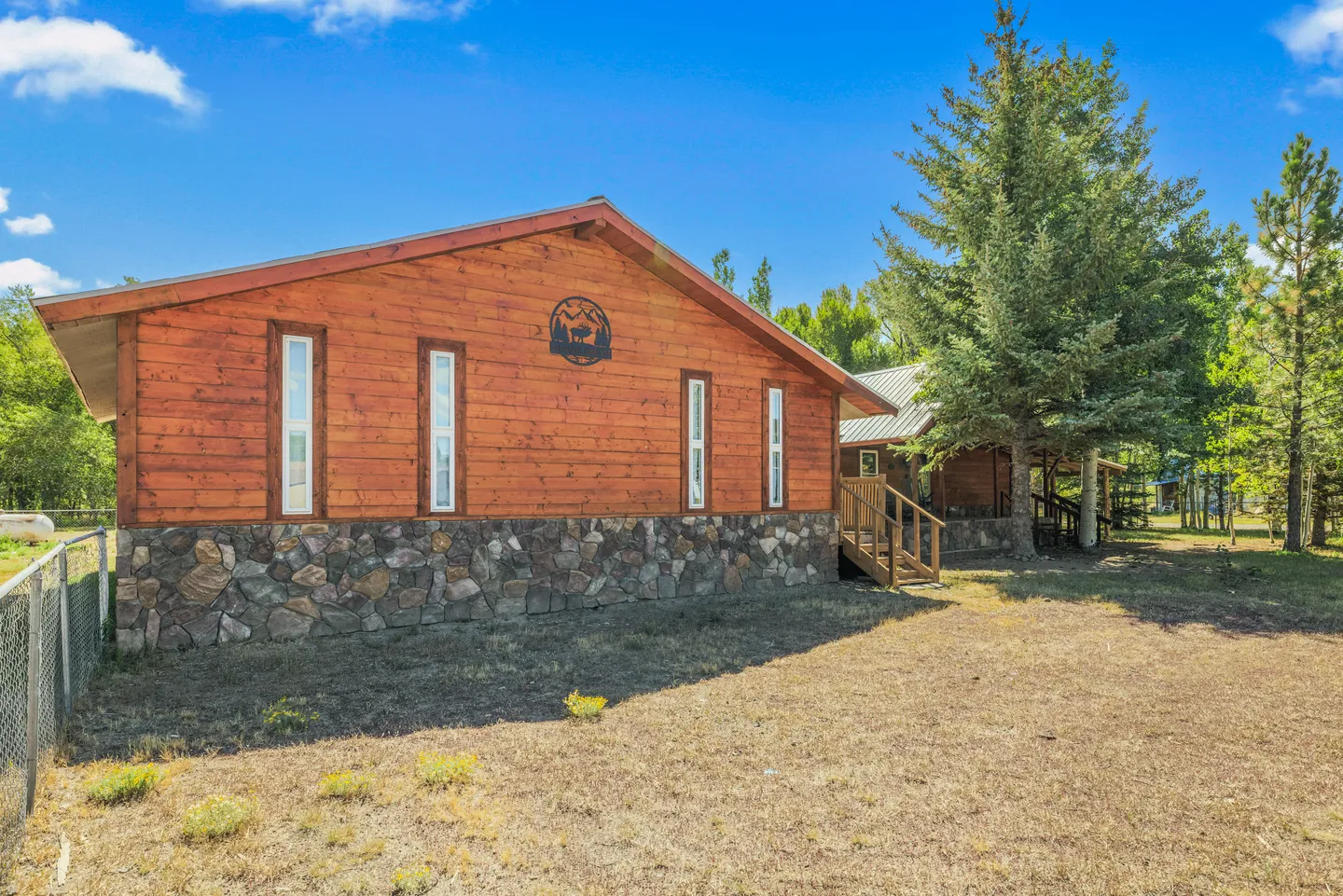 Exterior of a wood cabin with stone foundation and narrow vertical windows under a blue sky.