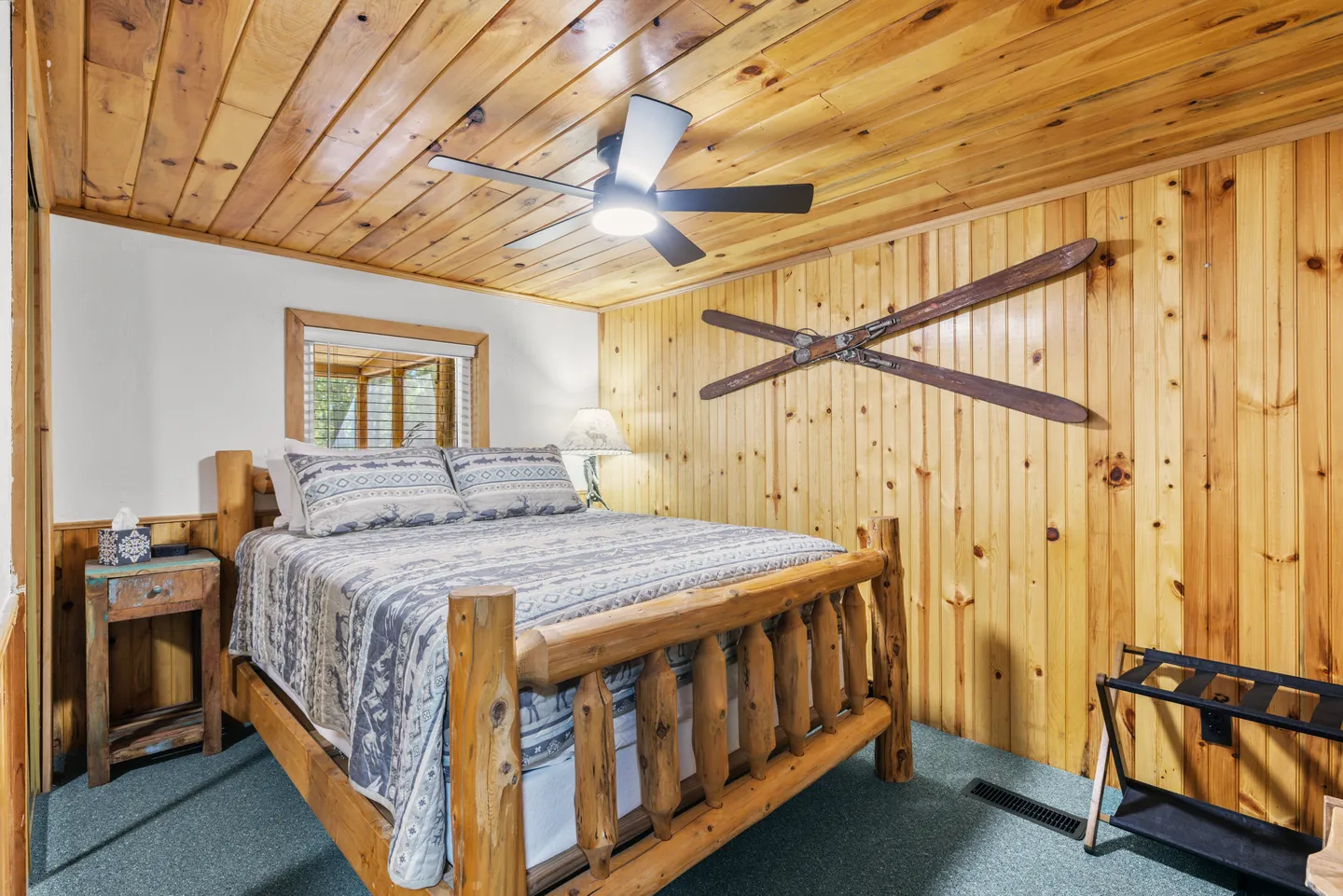 Bedroom with log frame bed, wood-paneled walls and ceiling, ceiling fan, and decorative skis on the wall.