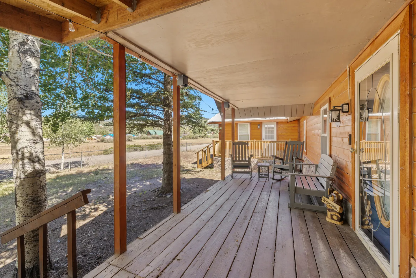 Covered wooden porch with outdoor rocking chairs and bench overlooking trees and a yard.