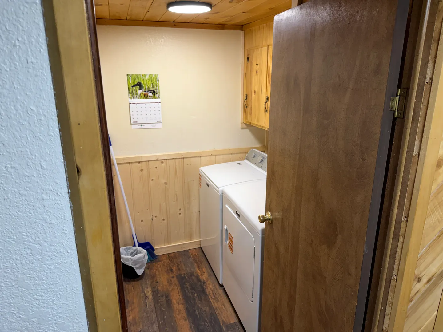 A laundry closet featuring a side-by-side white washer and dryer, wood plank flooring, wainscoting, and wooden cabinets.