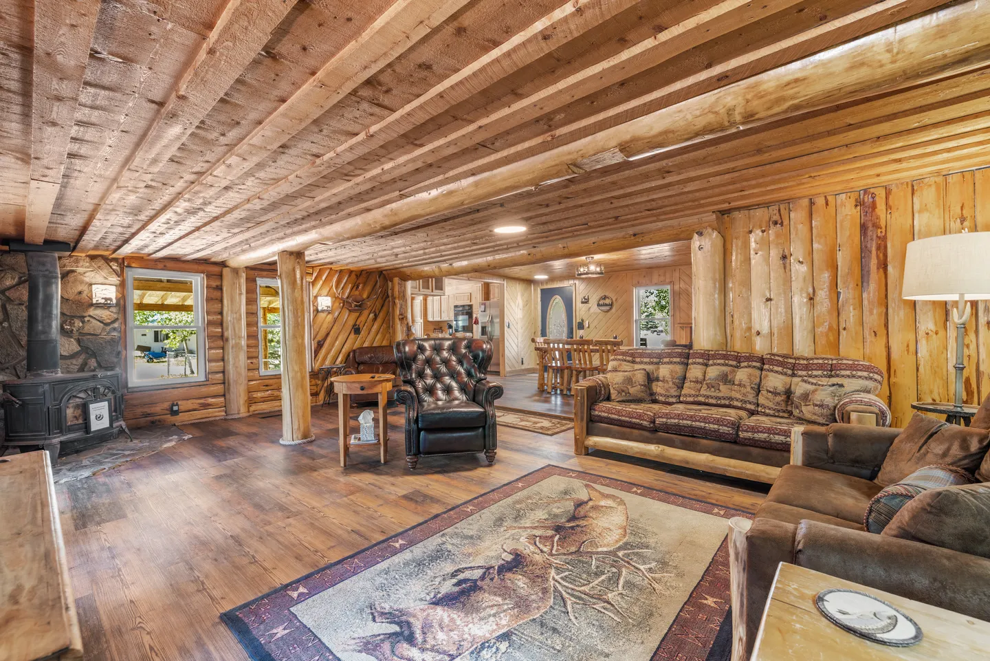 Living room with wood-paneled walls and ceiling beams, leather and fabric seating, and a wood-burning stove.