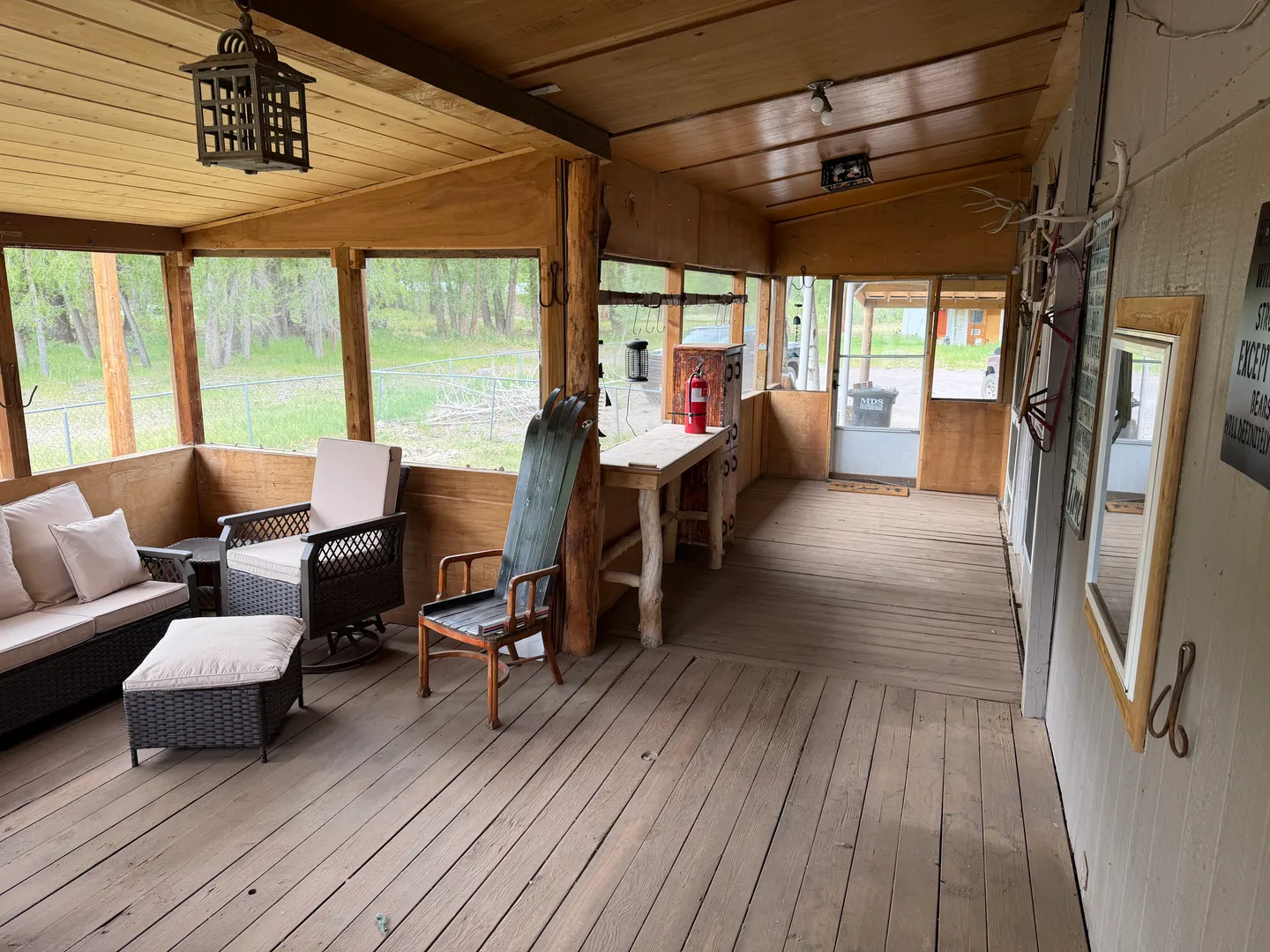 A long screened-in porch with wood floors, a wood ceiling, and casual seating overlooking trees outside.