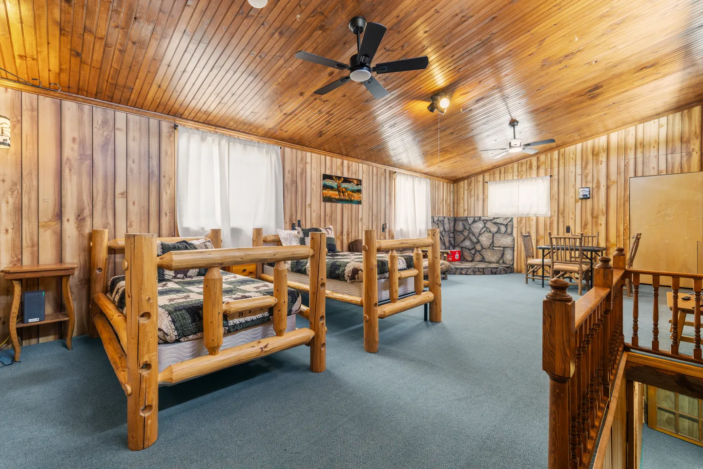 Upstairs bedroom area with rustic log-frame beds, wood-paneled walls, slanted wood ceiling, and blue carpet.