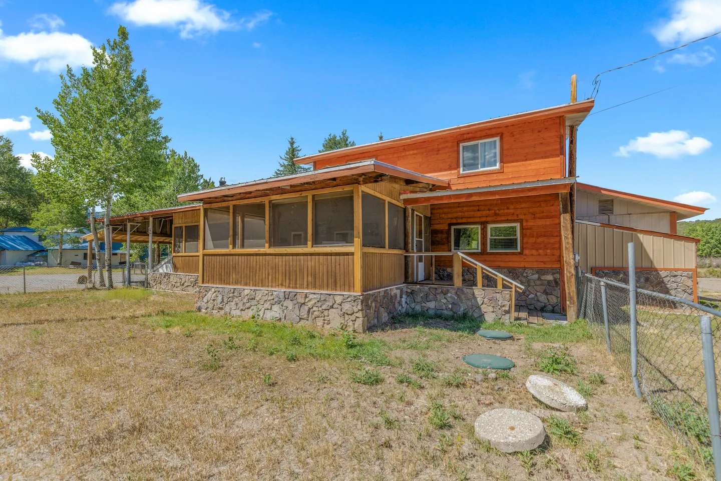 Exterior view of a wood-sided house with a screened porch and stone foundation under a blue sky.