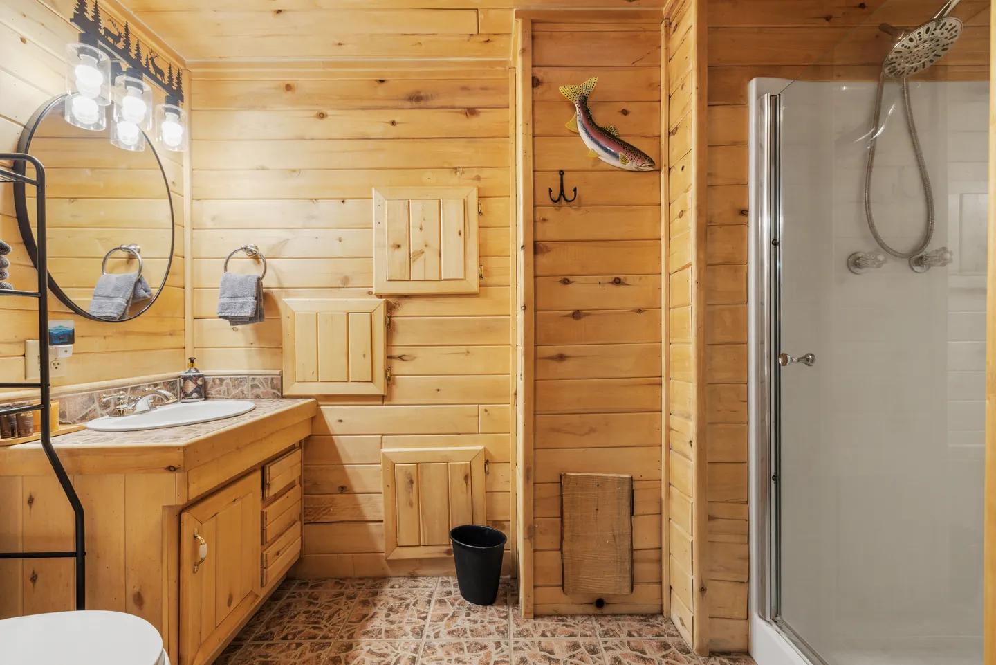 Bathroom featuring wood-paneled walls, a vanity with a sink and round mirror, tiled flooring, and a walk-in shower with a glass door.