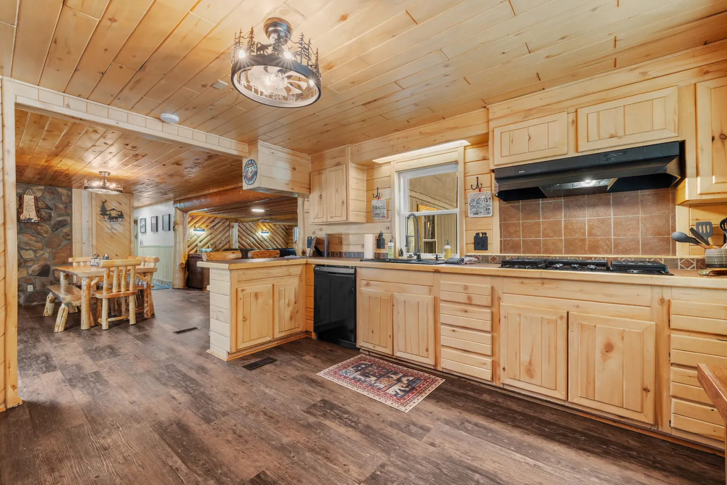 Kitchen with light wood cabinetry, wood-paneled walls and ceiling, dark flooring, and an open view into the dining area.