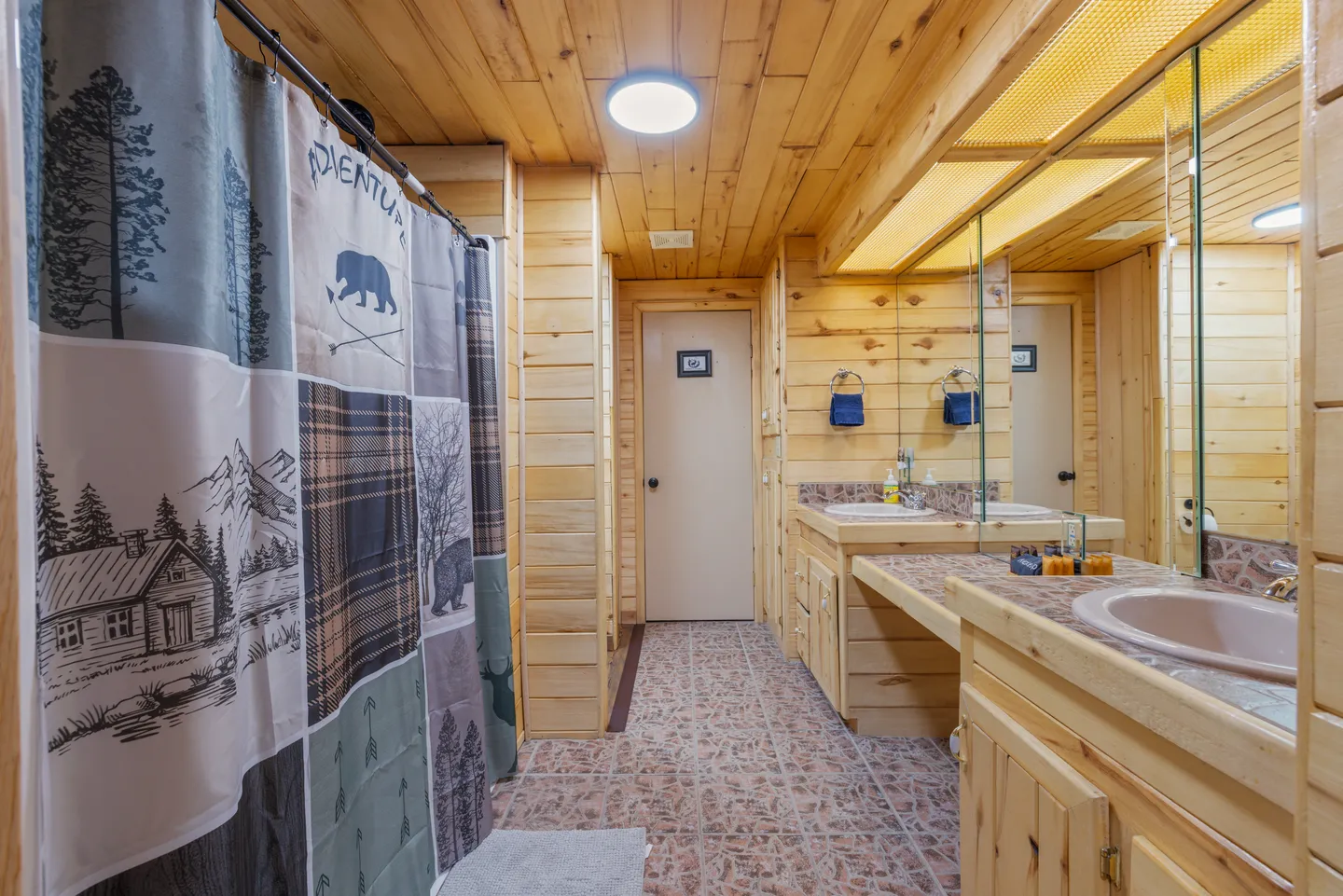 Bathroom with wood-paneled walls and ceiling, a long vanity with dual mirrors, tiled flooring, and a patterned shower curtain.