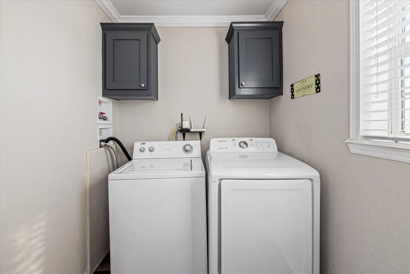 Dedicated indoor laundry space with a white washer, white dryer, and dark wall-mounted upper cabinets.