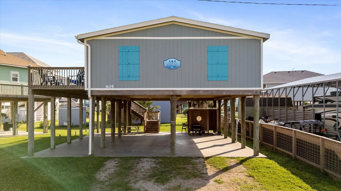 Exterior view of an elevated coastal home on pilings with blue shutters and a covered ground-level area.