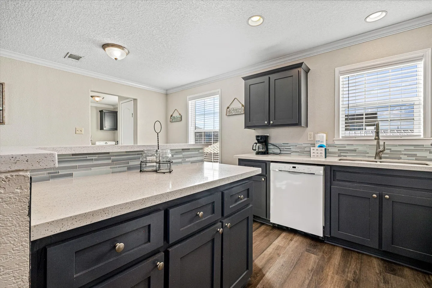 Kitchen counter and dark gray cabinets with white countertops, a dishwasher, and windows with blinds.