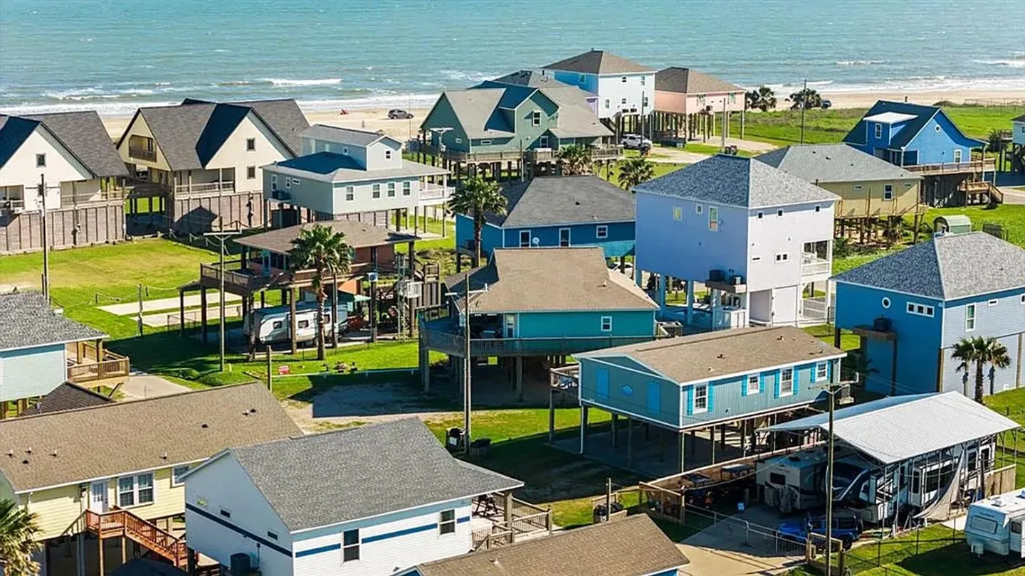 Aerial view of colorful stilt beach houses in a coastal neighborhood near the ocean and beach.
