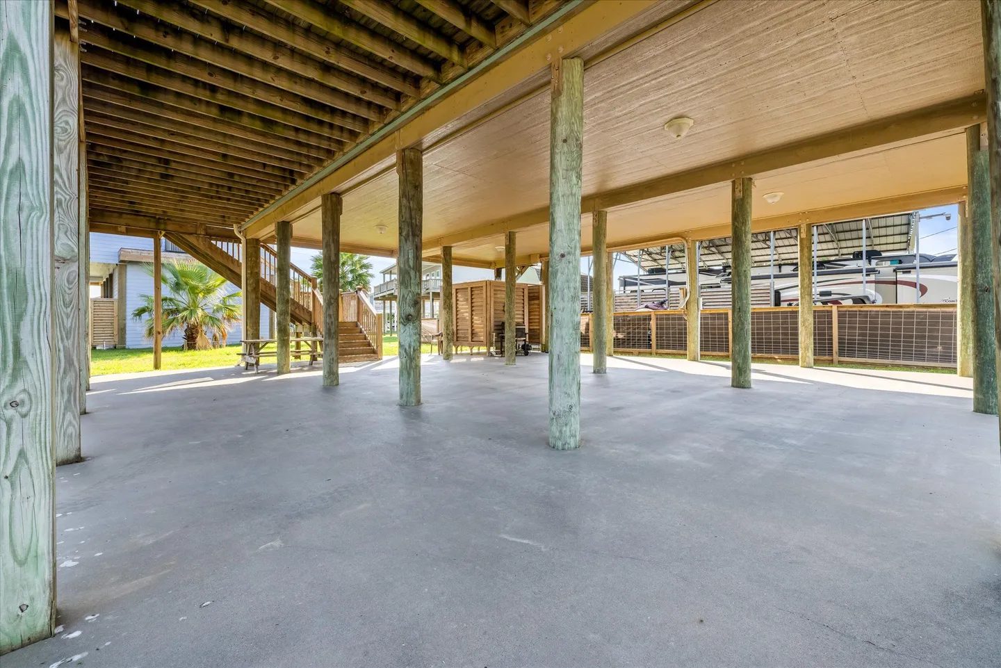 Open, covered concrete patio area supported by wooden pilings beneath a stilt home.