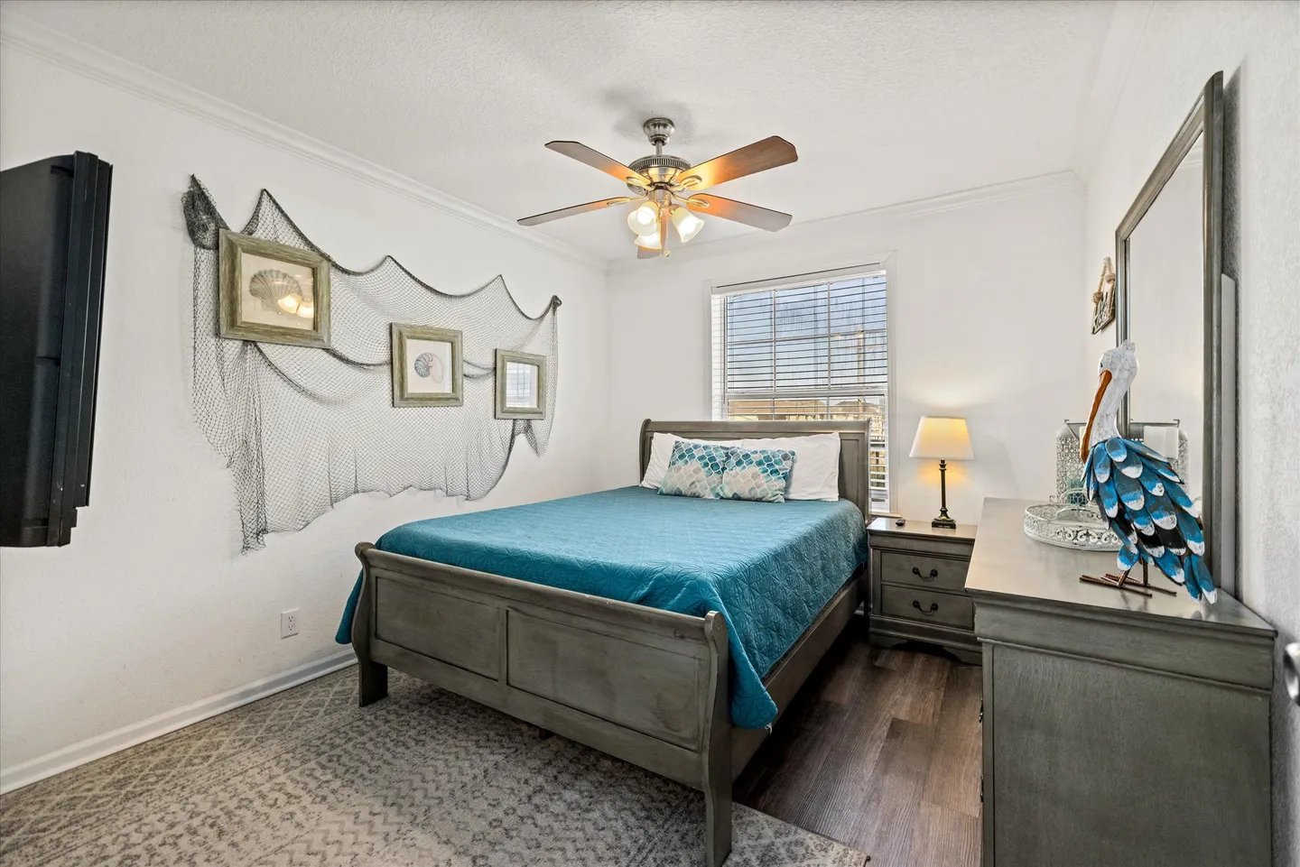 Bedroom with a wooden sleigh bed, matching furniture, coastal wall decor with a net, and a ceiling fan.